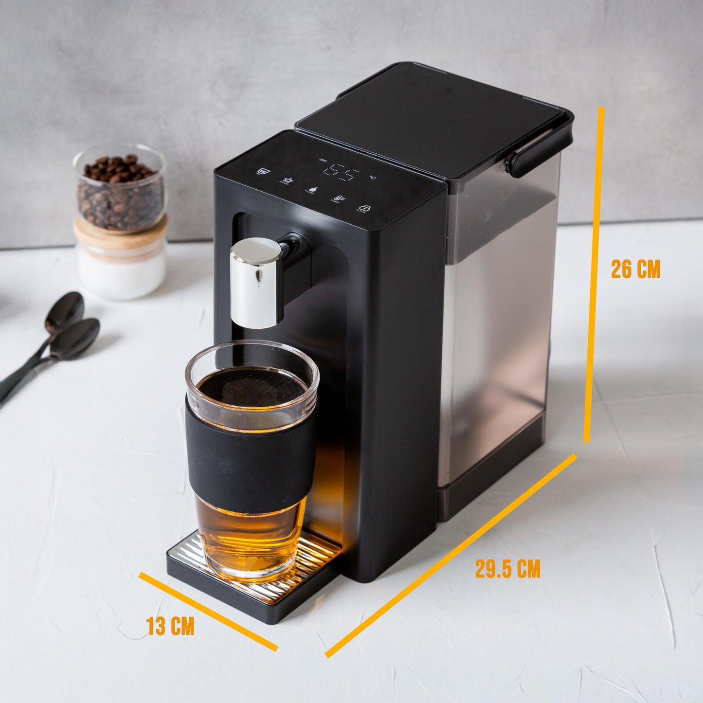 Black and silver coffee machine with a glass of coffee on a white surface, with measurements indicated.