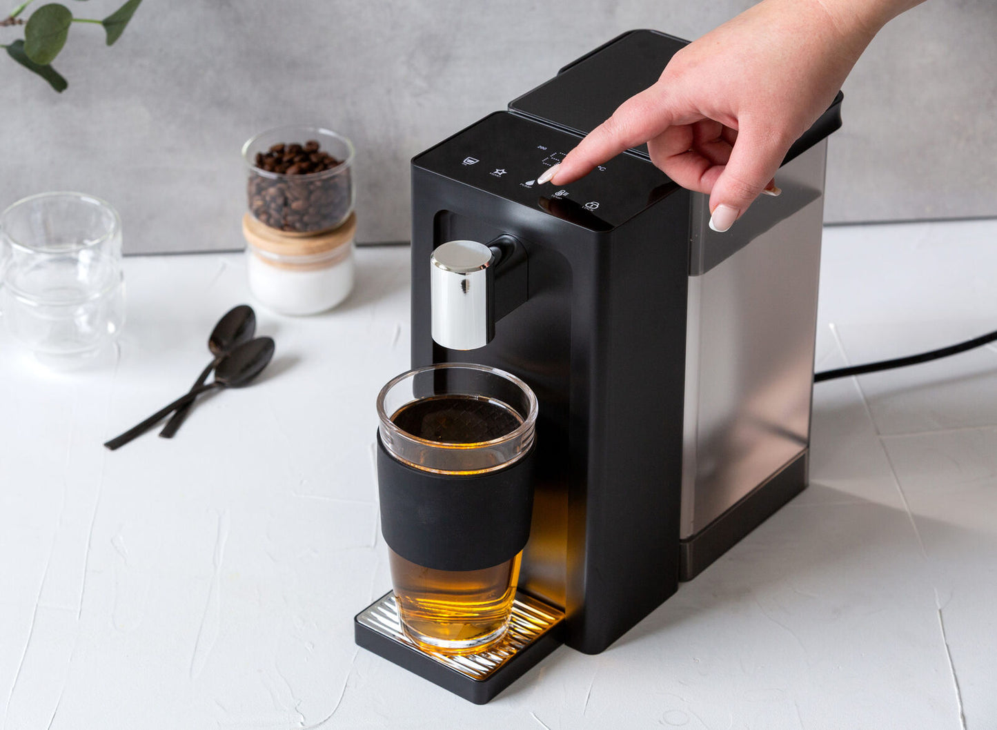Black coffee machine dispensing a glass of coffee on a white countertop.
