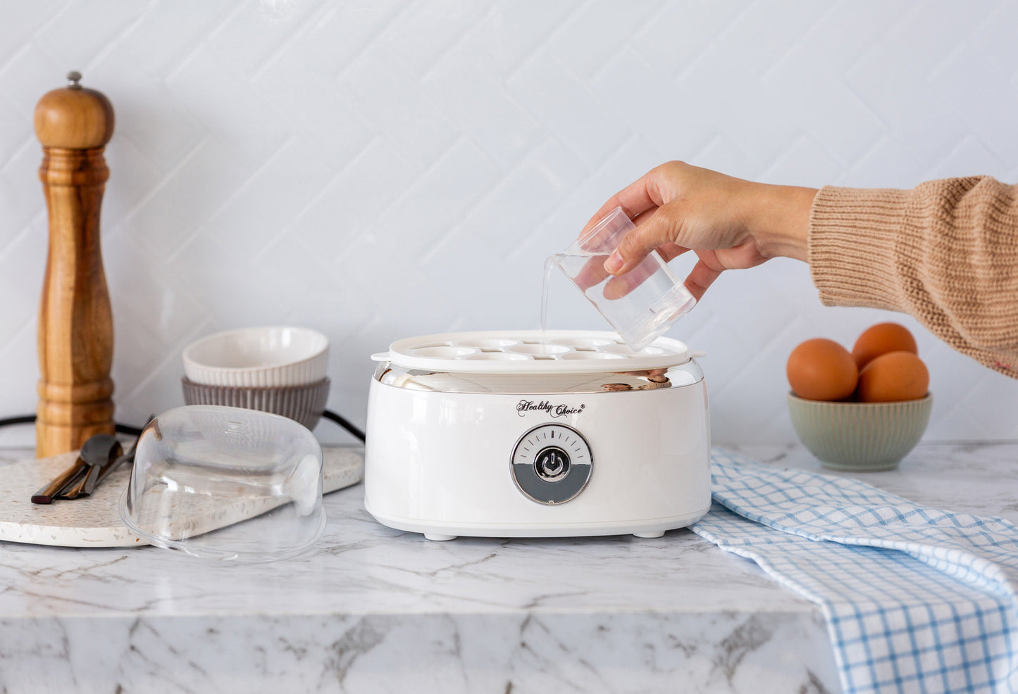 Person using a white appliance on a kitchen counter with fruits and kitchen items in the background.