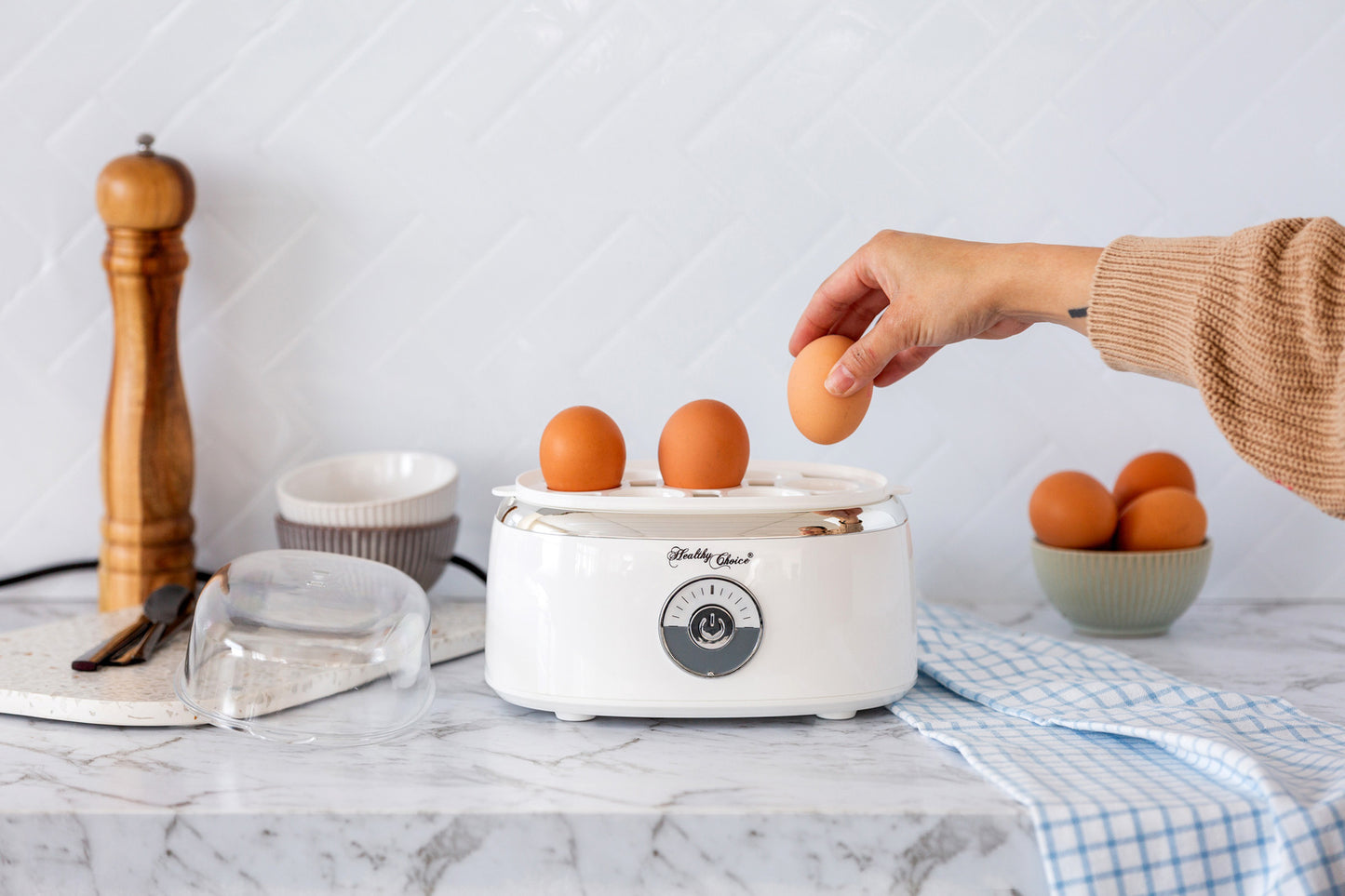 Person placing eggs into a white egg cooker on a kitchen counter.
