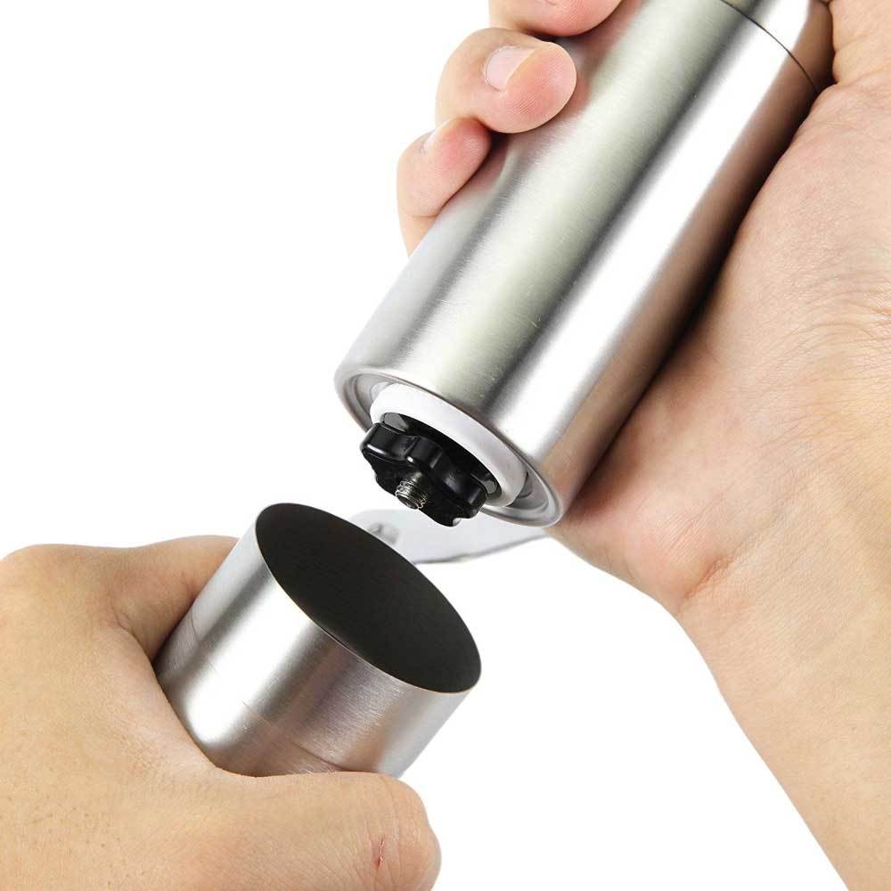 Metallic pepper grinder being held by a hand on a white background