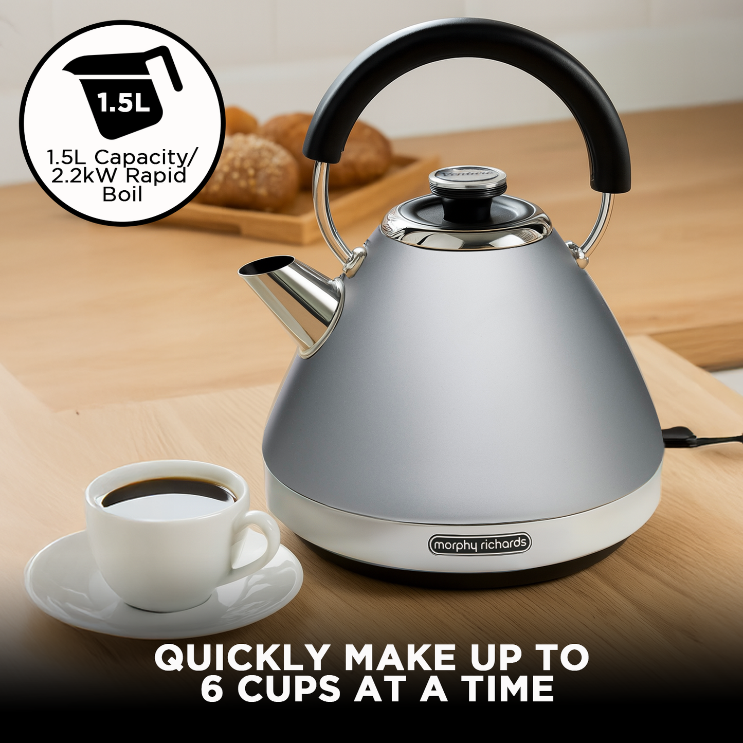 Silver electric kettle with black handle on a wooden surface, next to a cup of coffee.