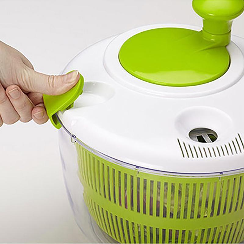Green and white salad spinner with a hand turning the handle on a white background