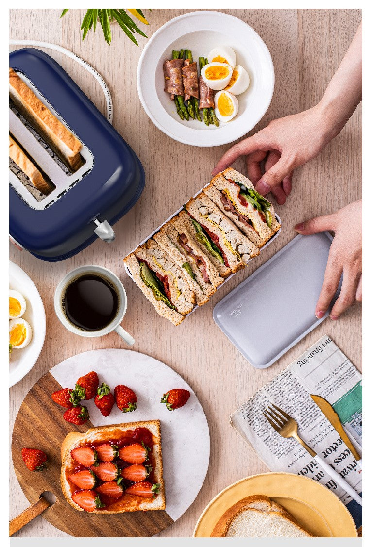 Breakfast scene with sandwiches, toast, coffee, and fruit on a table.