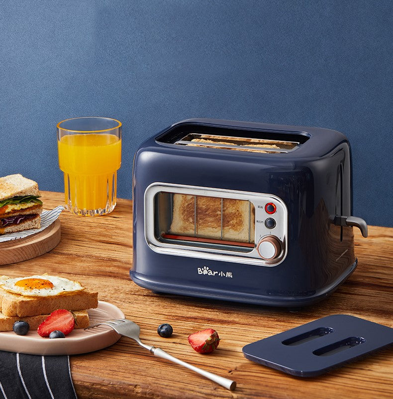 Navy blue toaster with slices of bread on a wooden table with a glass of orange juice and breakfast items.