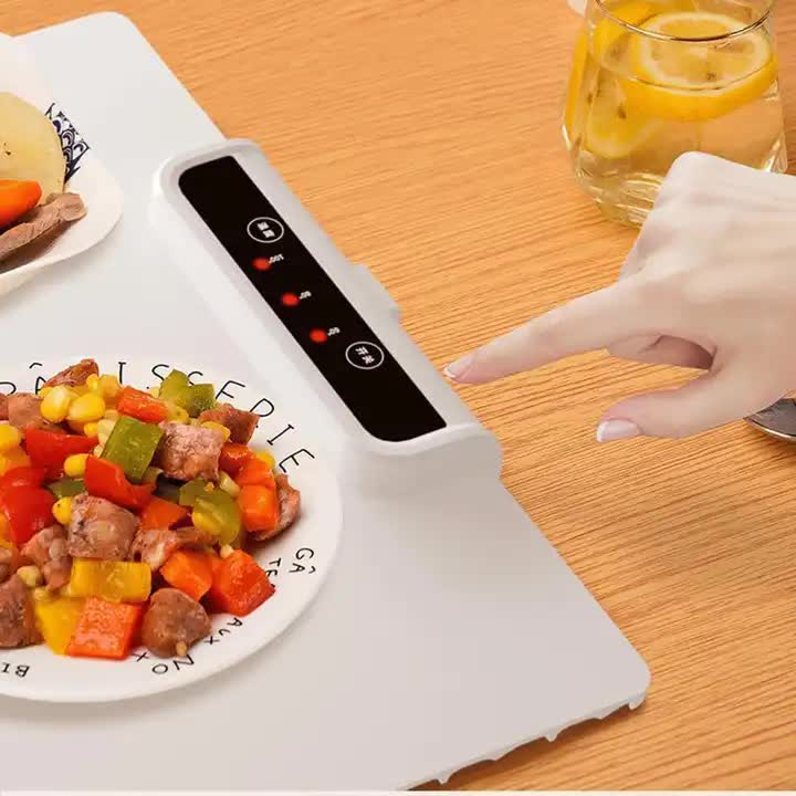 Hand using a small electronic device on a plate of food with a glass of lemon water in the background.