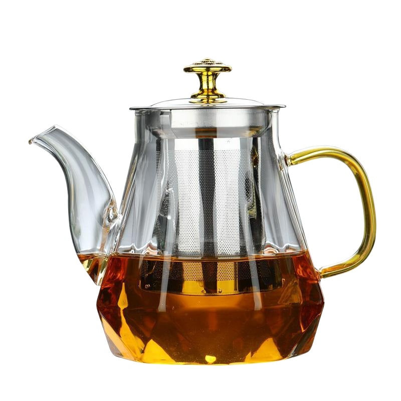 Clear glass teapot with gold handle and lid filled with tea on a white background
