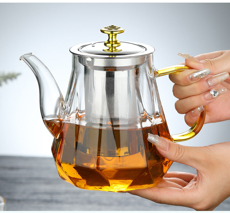 Glass teapot with a metal handle and lid held by a hand, filled with tea.