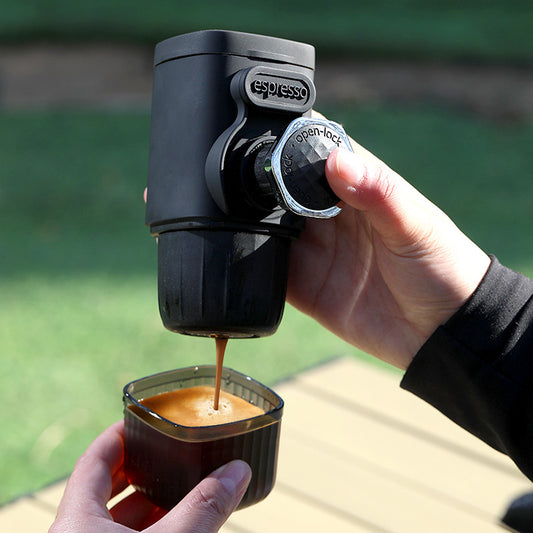 Hand using a portable espresso machine to pour coffee into a cup outdoors.