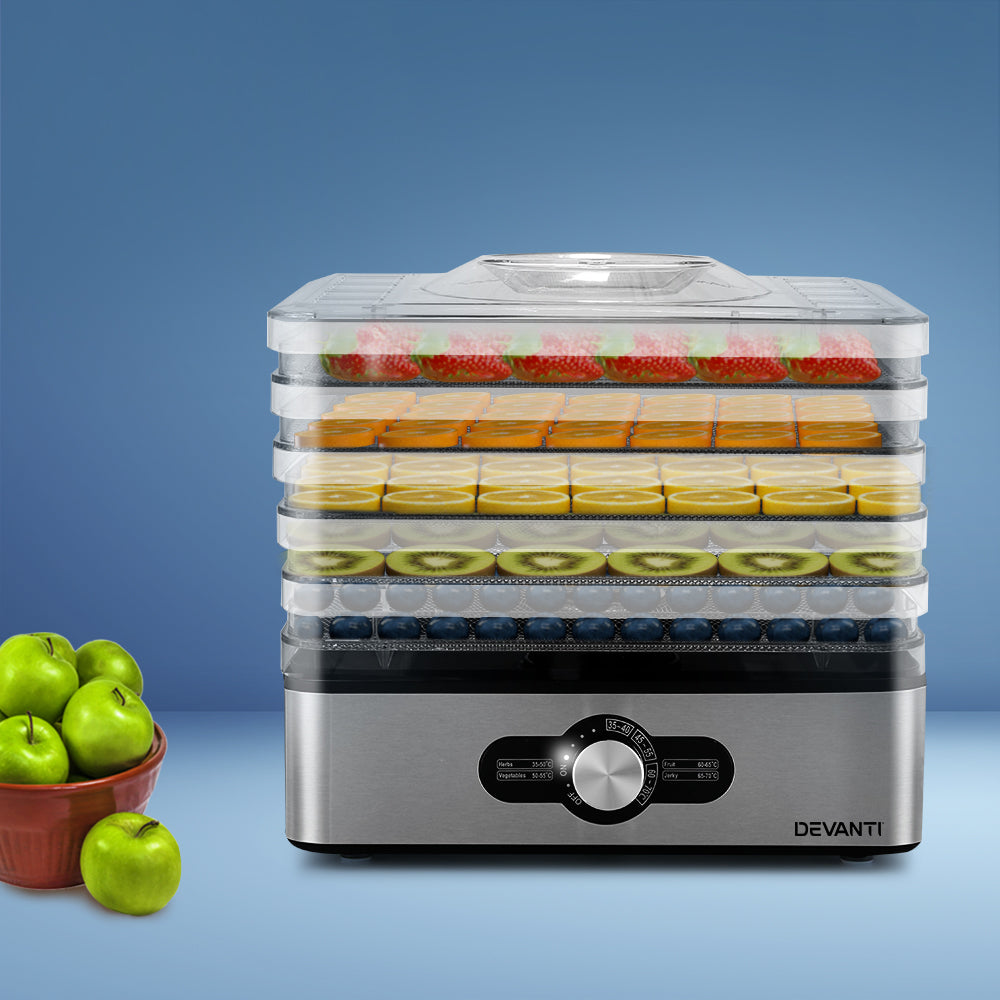 Dehydrator with food on trays next to a bowl of green apples on a blue background