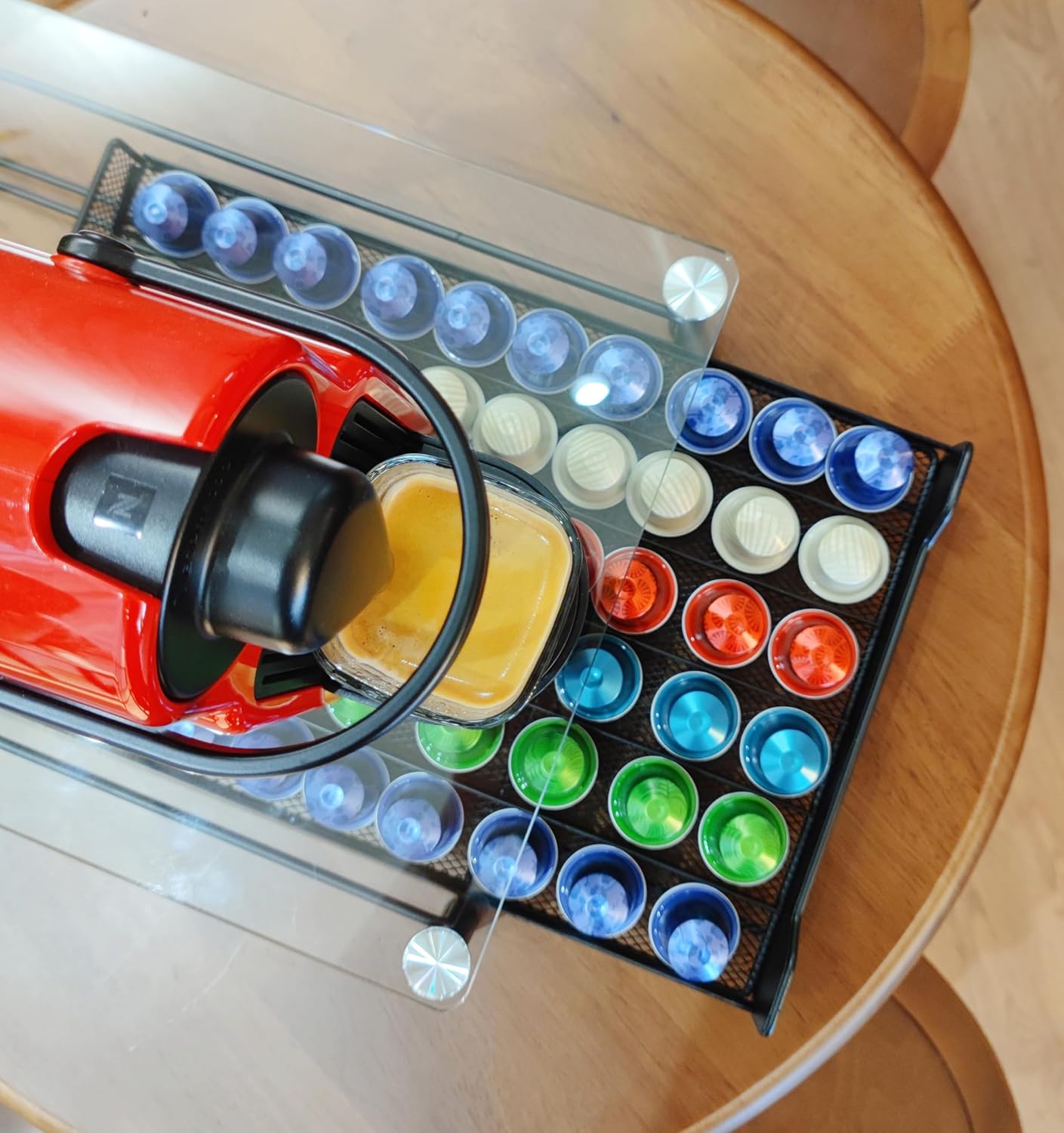 Red coffee machine being used to fill colorful coffee pods on a wooden table.