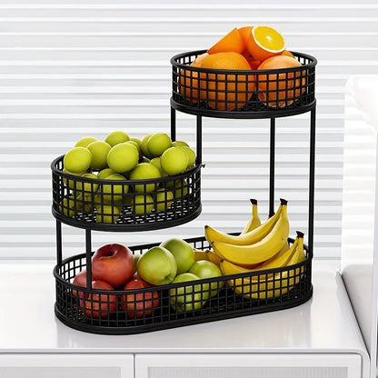 Three-tiered black fruit basket organizer with apples, bananas, and oranges on a white surface.