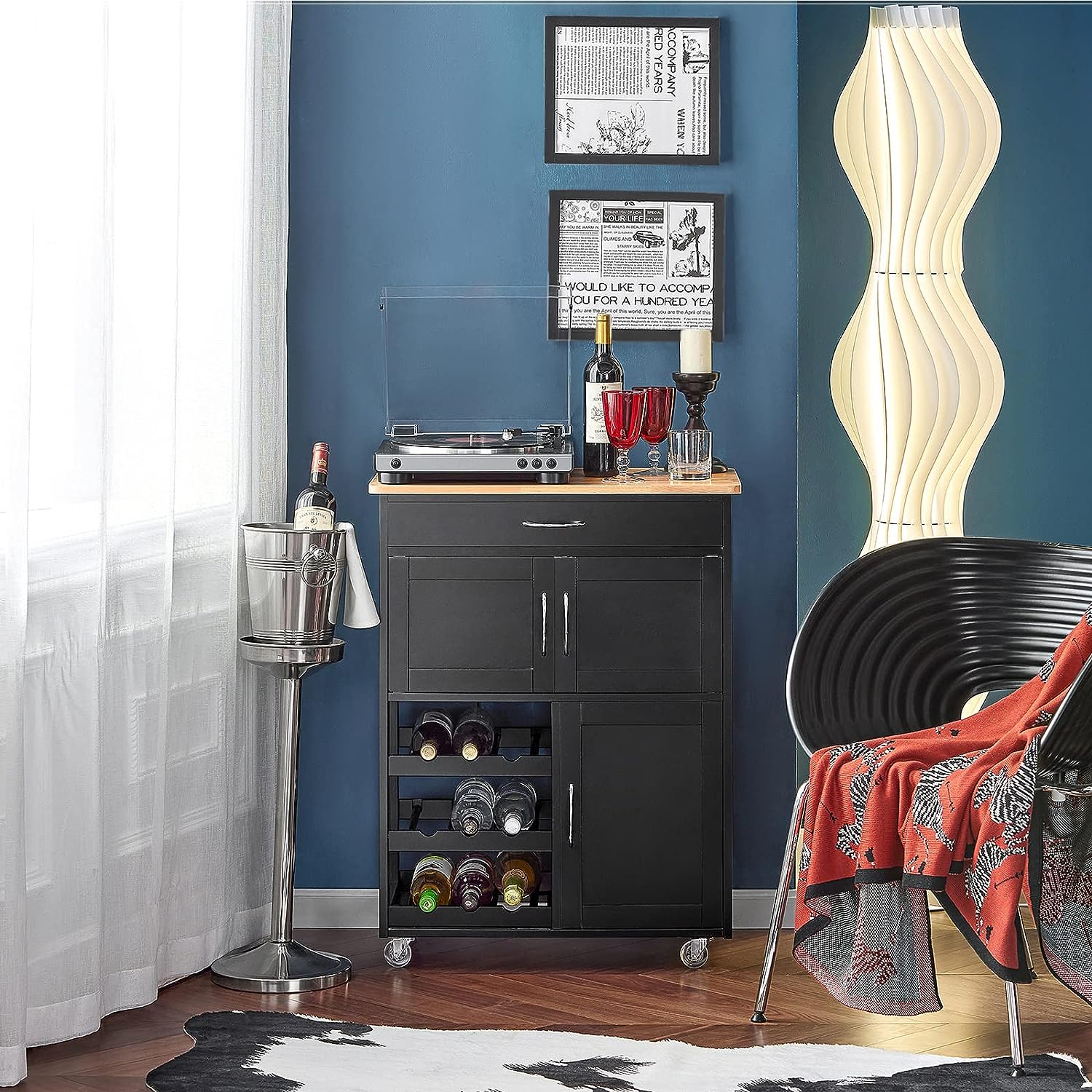 Black bar cart with wine bottles and glasses against a blue wall.