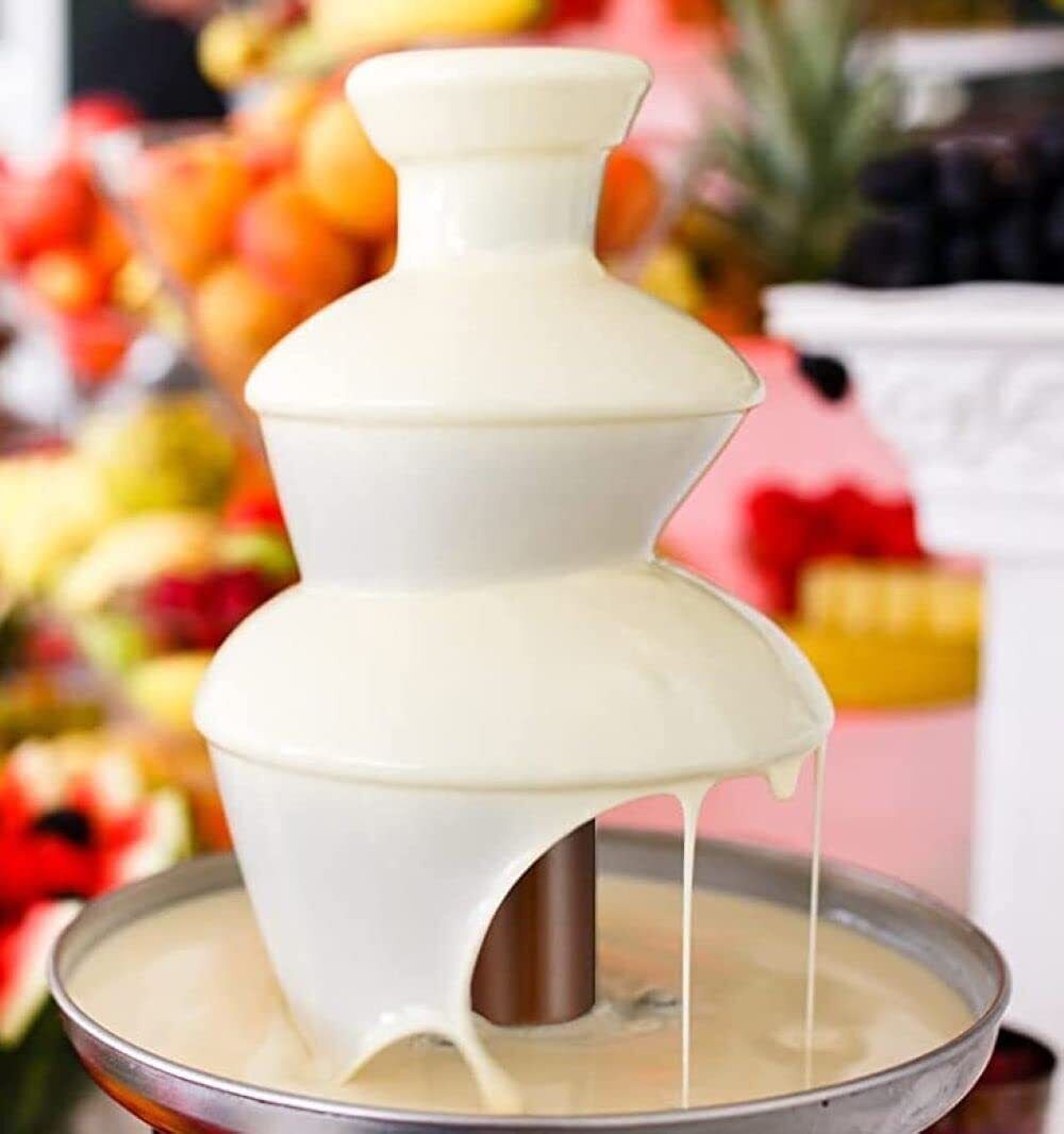 White chocolate fountain with a blurred fruit background