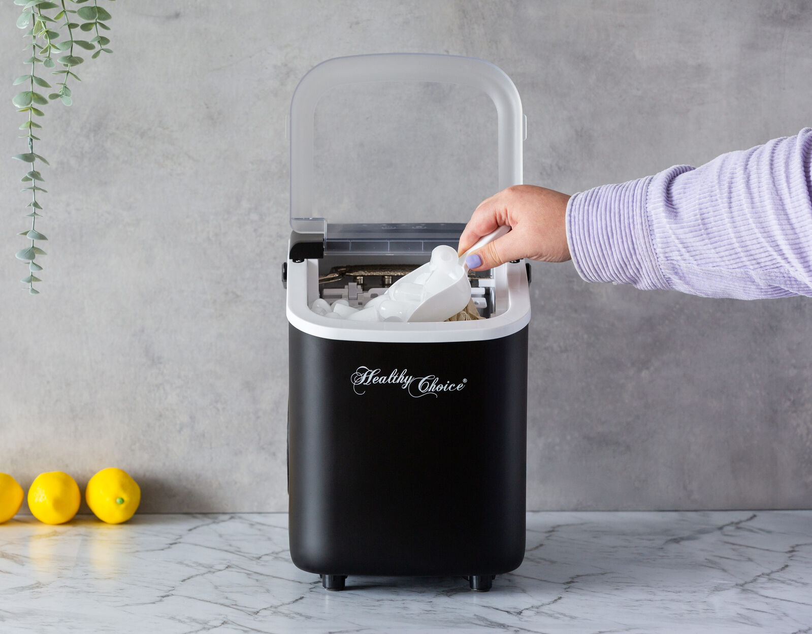 Person using a portable ice maker with lemons on a marble surface.