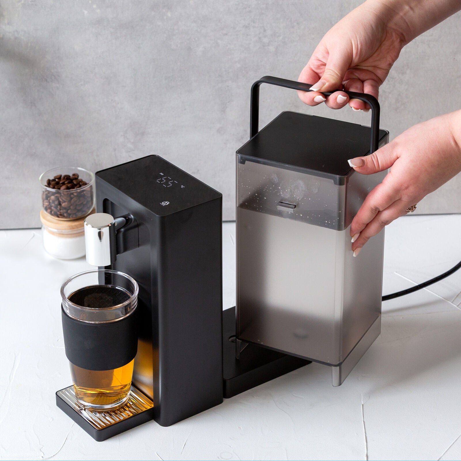 Coffee machine dispensing coffee into a glass on a white surface.