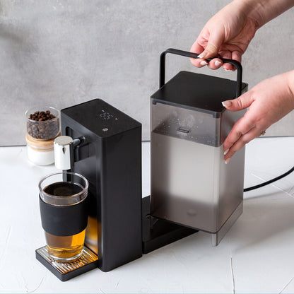 Coffee machine dispensing coffee into a glass on a white surface.