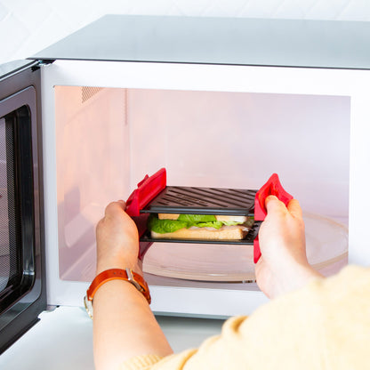 Person using a red silicone glove to open a microwave with food inside.