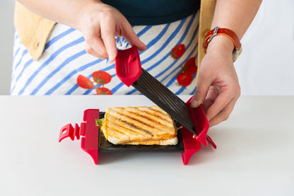 Person using a red and black sandwich cutter on a grilled cheese sandwich.