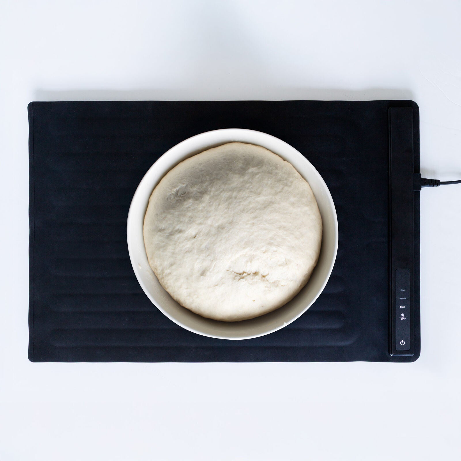 Bowl of dough on a black heating pad with digital display