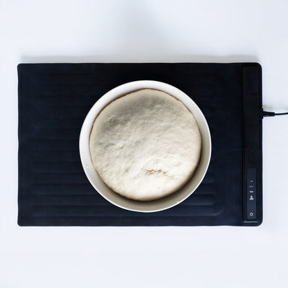 Bowl of dough on a black heating pad with digital display