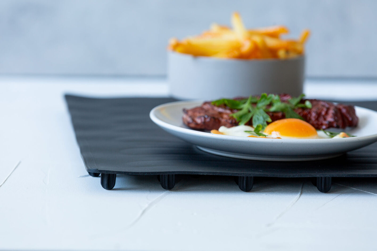 Plate of food with an egg and greens on a white surface, with a bowl of fries in the background.
