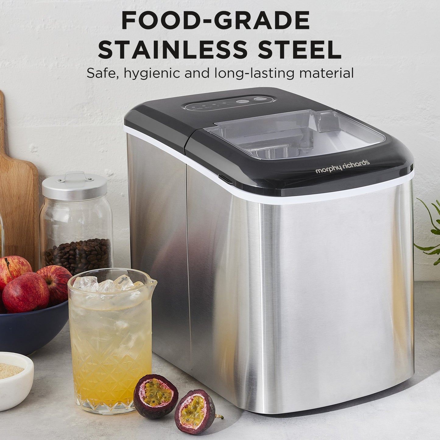 Stainless steel ice maker with a glass of iced drink and fruit on a countertop.