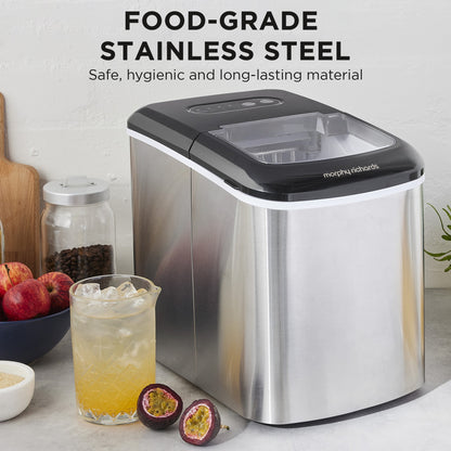 Stainless steel ice maker with a glass of iced drink and fruit on a countertop.