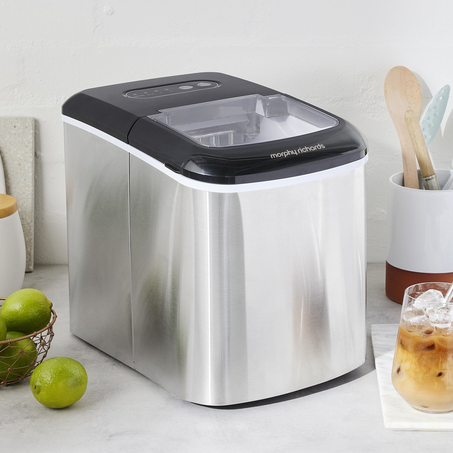 Morphy Richards ice maker on a kitchen counter with limes and a glass of iced coffee.