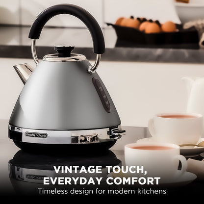 Silver kettle with black handle on a kitchen counter, surrounded by coffee cups.