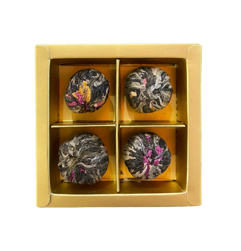 Four tea balls in a gold box on a white background