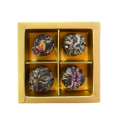 Four tea balls in a gold box on a white background