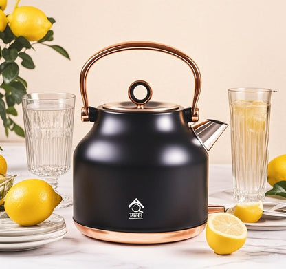 Black electric kettle with copper handle and base on a table with lemons and glasses.