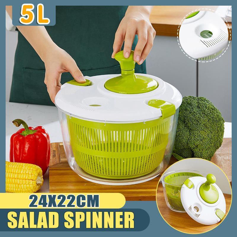 Green salad spinner with a person using it, surrounded by vegetables on a wooden surface.