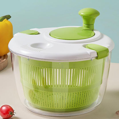 Green and white salad spinner on a light blue background with vegetables around.