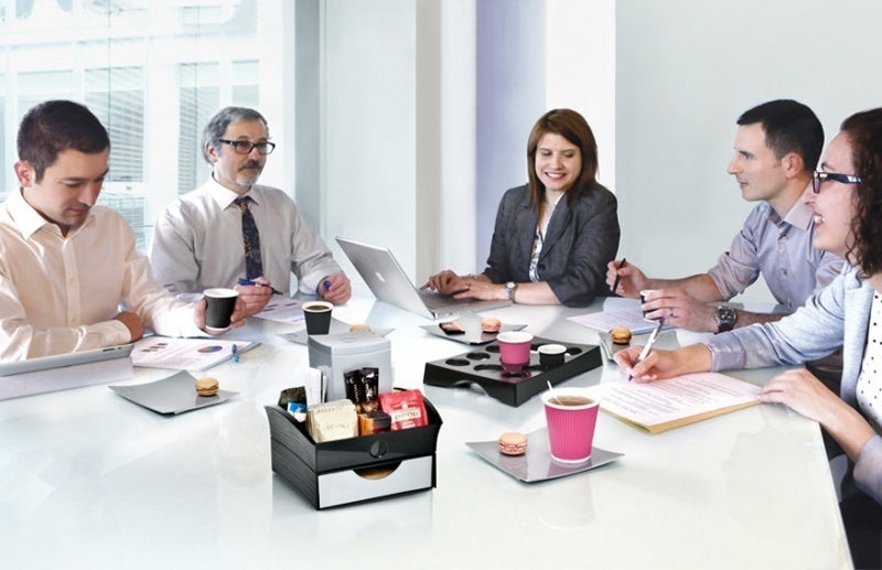 Group of people in a meeting at a conference table with coffee cups and snacks.