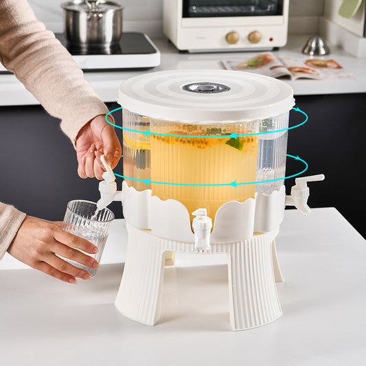 Person pouring tea from a white tea infuser into a glass on a kitchen counter.