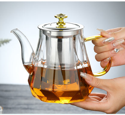 Glass teapot with a metal handle and lid held by a hand, filled with tea.