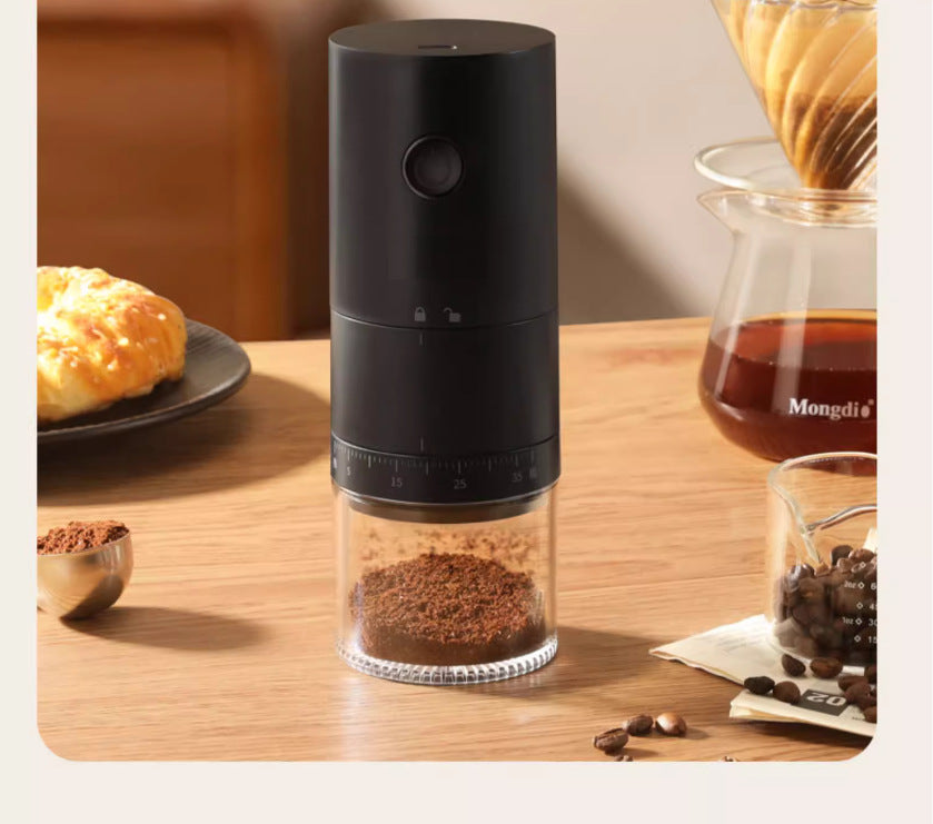 Black coffee grinder on a wooden table with coffee beans and a cup in the background