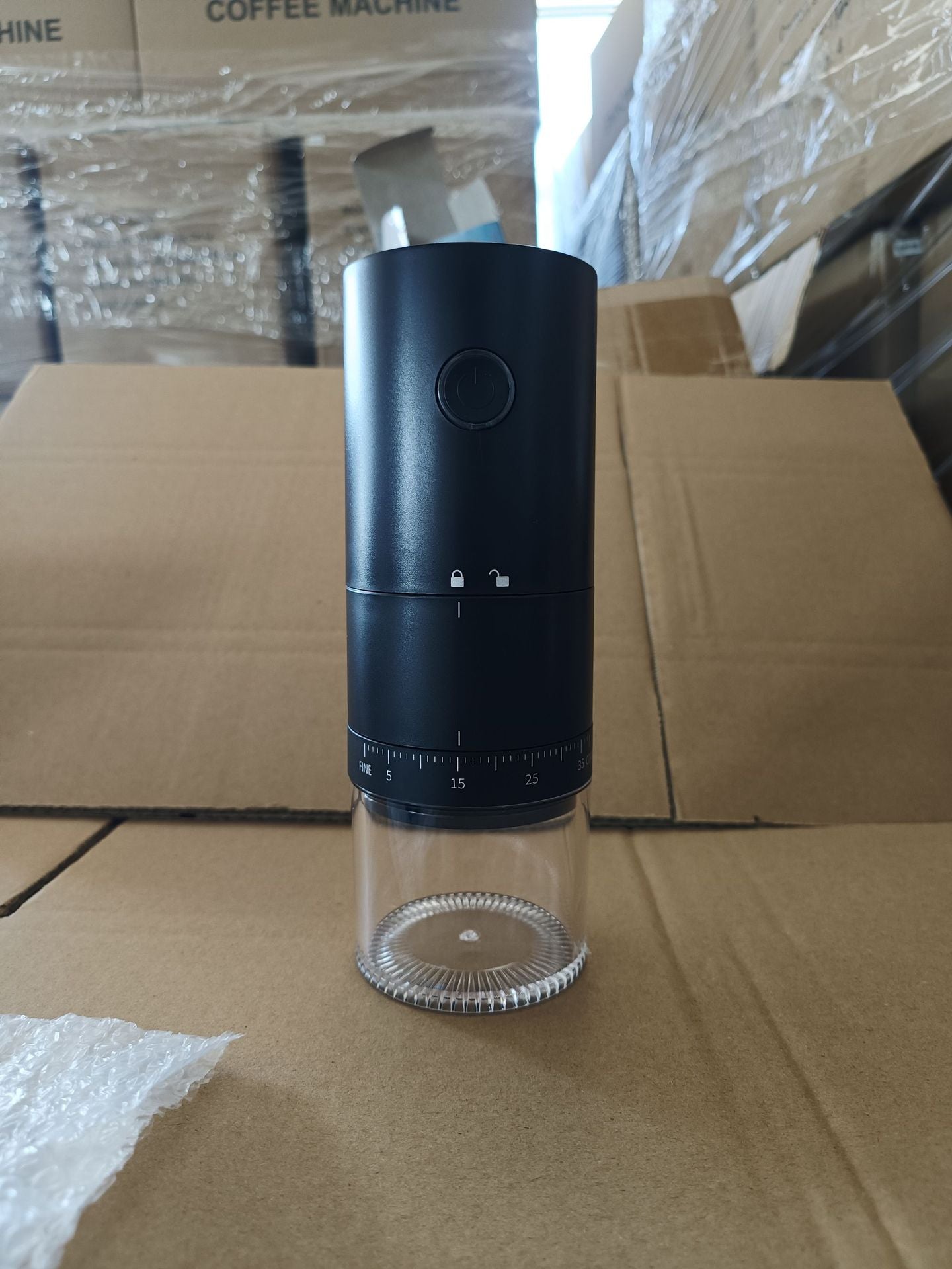 Black and clear pepper grinder on a cardboard surface with boxes in the background