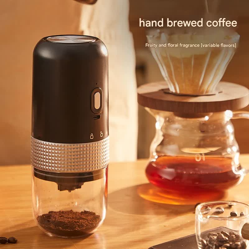 Handheld coffee grinder with coffee beans and a brewing setup in the background.