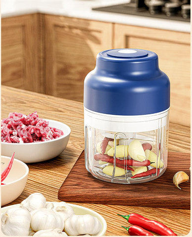 Blue and transparent kitchen grinder on a wooden cutting board with minced meat and garlic in the background.
