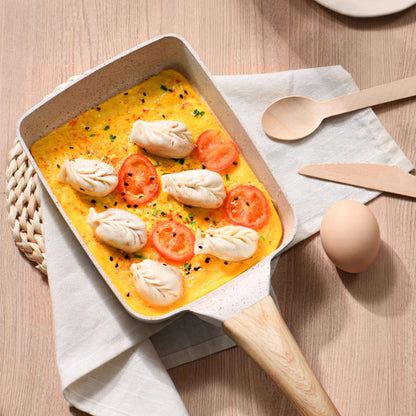 Square pan with yellow dish, tomatoes, and dumplings on a wooden surface with kitchen utensils.