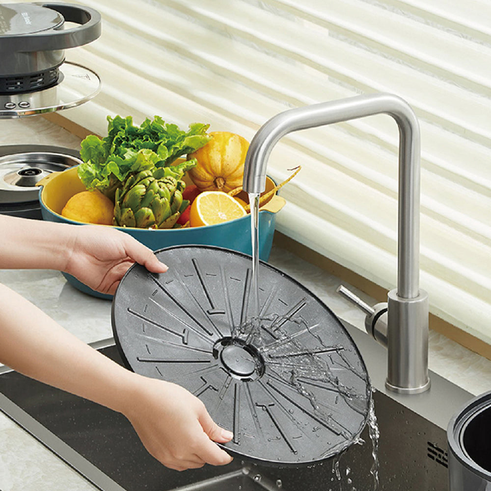Person using a black kitchen sink strainer with running water, surrounded by fruits and vegetables.