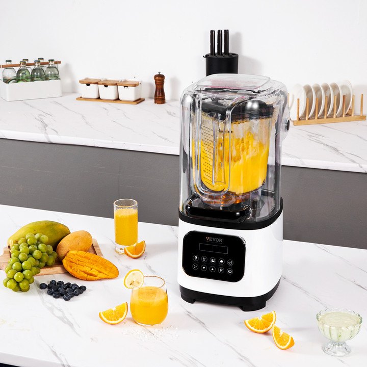 Blender with a yellow liquid on a kitchen counter with fruits and juice.
